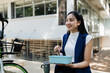 Asian young businesswoman bike to work for eco friendly green energy and eat lunch using box lunch prepared from home. while commuting in city. Eco friendly