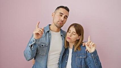 Poster - Beautiful couple in denim shirts, standing upset, pointing up in despair over pink isolated background. their sad, unhappy faces indicating a troubling direction.