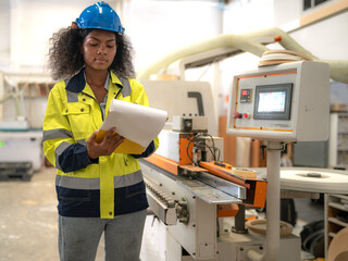 Wall Mural - Skill afro multiracial worker working in wooden furniture small business factory. Young adult woman checking auto machine by checklist in carpentry workshop. Professional woodwork builder occupation