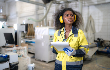 Wall Mural - Skill afro multiracial worker working in wooden furniture small business factory. Young adult woman checking auto machine by checklist in carpentry workshop. Professional woodwork builder occupation