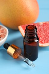 Wall Mural - Grapefruit essential oil in bottle, pipette and fruits on light blue wooden table, closeup