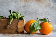 © ADDICTIVE STOCK - Ripe oranges with fresh green leaves attached are displayed, some resting on a textured surface and others nestled in a wooden crate, evoking a sense of fresh harvest