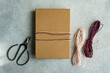 © ADDICTIVE STOCK - A simple yet elegant gift wrapped in brown paper with a pink and white twine, alongside scissors and additional twine on a textured grey background
