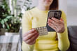 © Yura Yarema - Selective focus of young caucasian female using smartphone for reading, searching prescription, pill label text about information online, instructions side effects, pharmacy medicament concept