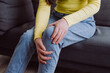 © Yura Yarema - Close up of unknown young caucasian female touching her knee feel pain and doing massage sitting alone on sofa at home. People health care bone problem, illness, cramps, rheumatism concept