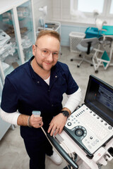 Wall Mural - Portrait of a sonographer working on a modern ultrasound machine in a clinic. Professional smiling modern adult ultrasound medicine doctor