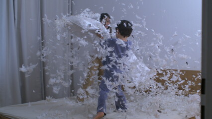 Wall Mural - Children engaged in pillow fight with feathers flying everywhere in the air captured in super slow motion at 1000 fps with a high speed camera while standing on bed