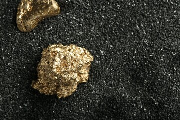 Wall Mural - Shiny gold nuggets on black sand, above view. Space for text