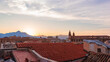 View of the mountains above the rooftops against the setting sun and pink cloudy sky. Red clay tiled roof in the old town of Palermo, Sicily, Italy