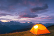 Glowing orange tent in the mountains under dramatic evening sky, mountains in the background. created generative ai