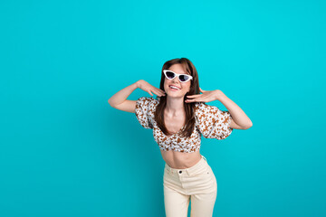 Sticker - Photo sweetie lady touching cheeks demonstrate her beautiful flawless face skin in sunglasses isolated on aquamarine color background