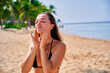 Portrait of satisfied young joyful happy smiling woman applying facial spf sunscreen while sunbathing and relaxing in the sun. Sunburn protection and healthy skin