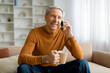 © Prostock-studio - Cheerful senior man sitting on couch, have phone conversation
