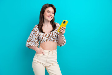 Wall Mural - Portrait of happy young woman in trendy glamour apparel buying clothes online using smartphone isolated on aquamarine color background