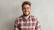 © MP Studio - A cheerful young man with a beard and a checkered shirt smiles brightly against a plain grey background.