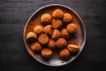 Poster - Chocolate truffles covered with cocoa powder on plate on black table. Top view.