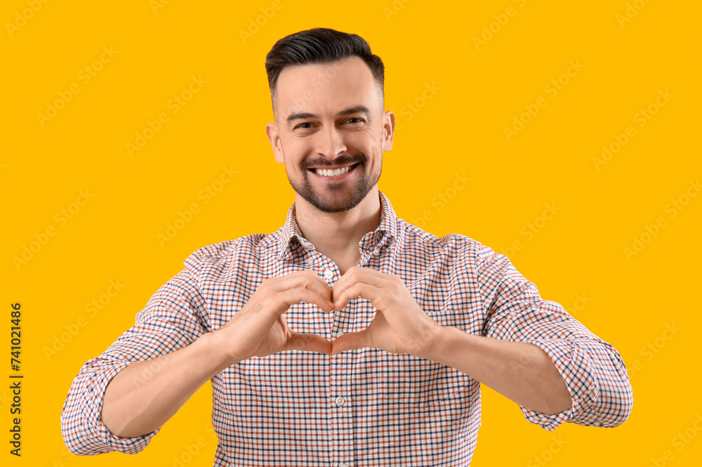 Handsome man making heart with his hands on yellow background
