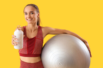 Canvas Print - Sporty young woman with bottle of water and fitball on yellow background