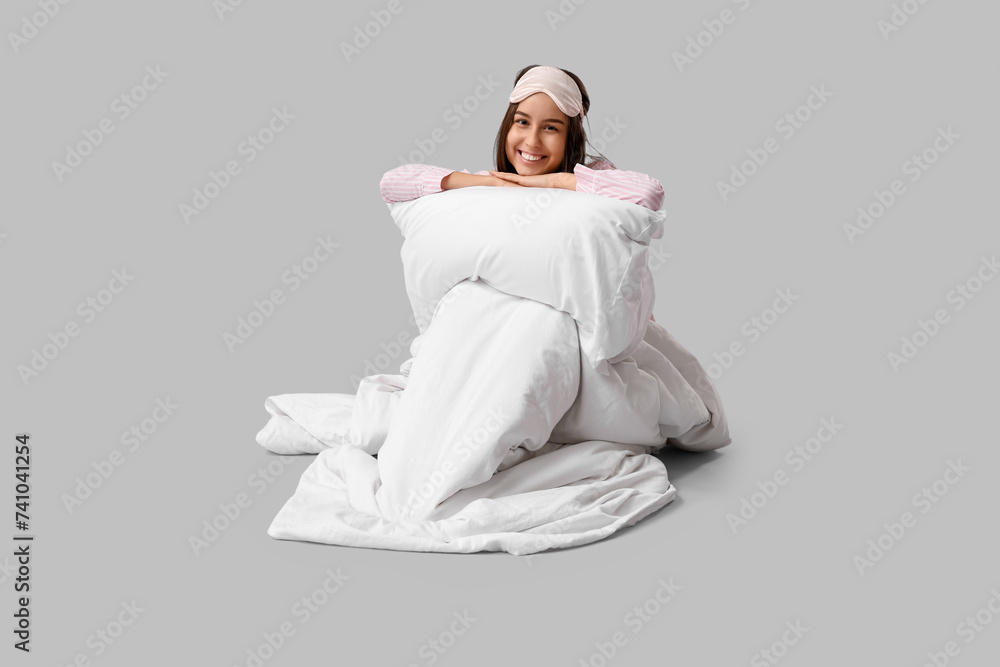 Pretty young woman with blanket and pillow on grey background