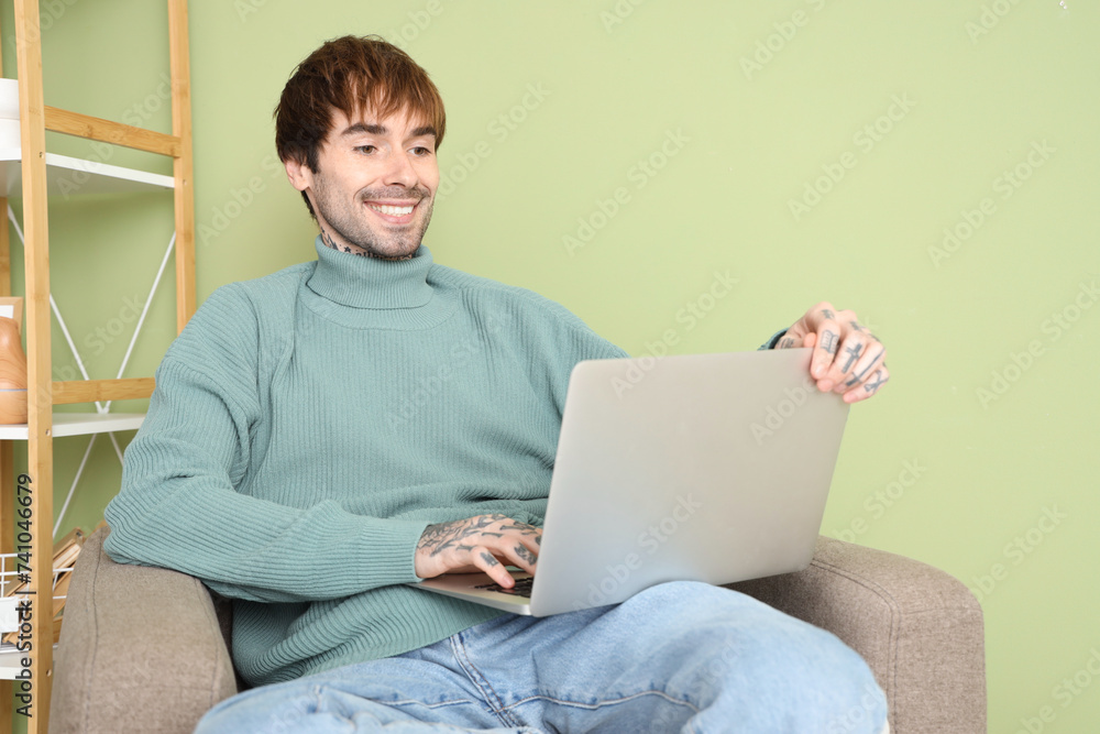 Handsome man using laptop in soft armchair at home