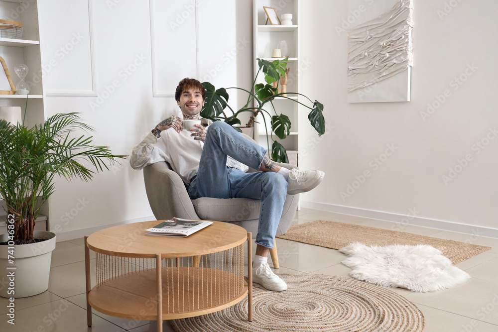 Handsome man with coffee cup resting in soft armchair at home