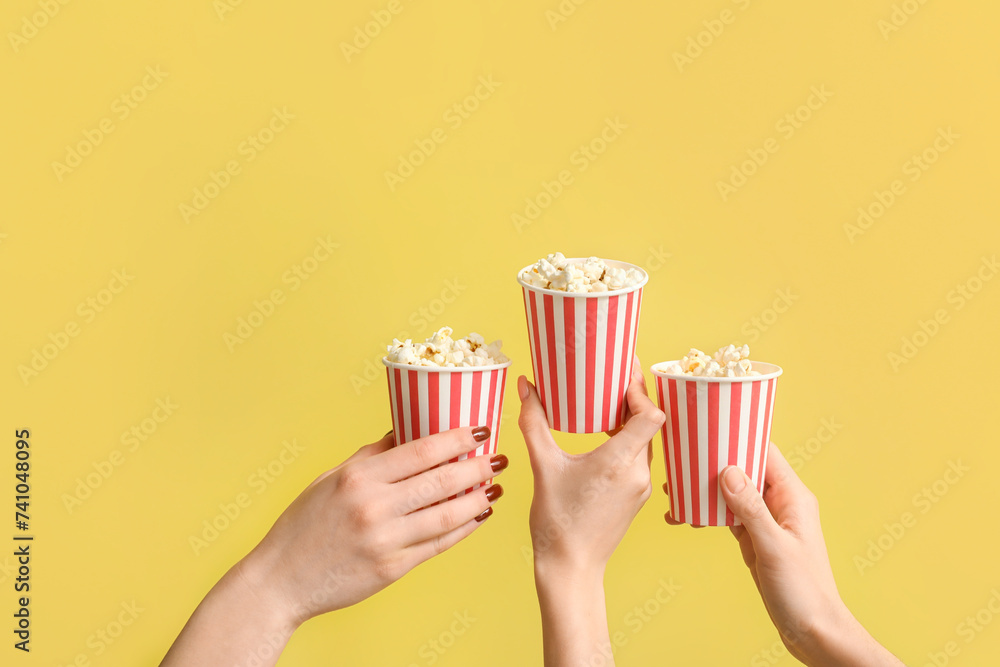 Hands holding buckets with popcorn on yellow background