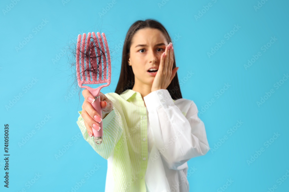 Shocked young woman with hair loss problem on blue  background