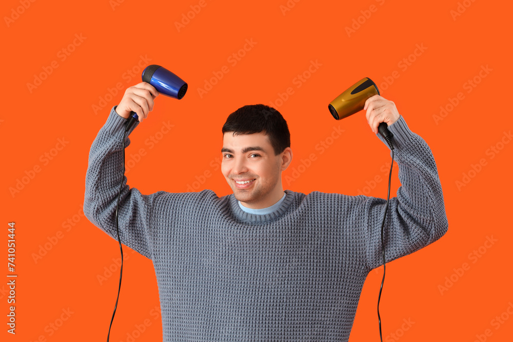 Handsome young man with hair dryers on orange background