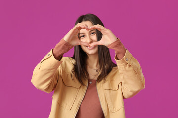 Poster - Beautiful young woman showing heart gesture on purple background. Valentine's Day celebration