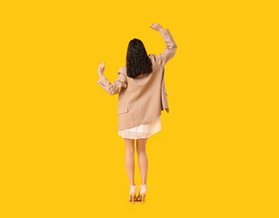 Wall Mural - Young woman in stylish white dress and jacket dancing on yellow background, back view