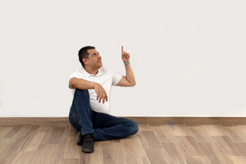 Wall Mural - Dark-skinned Latino 40-year-old man points to white wall as space for message of promotions and discounts