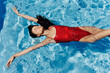 © SHOTPRIME STUDIO - Young woman in the pool in a red swimsuit with a beautiful smile lying on the water and swimming in the sun swimming in the pool, the concept of relaxing on vacation.