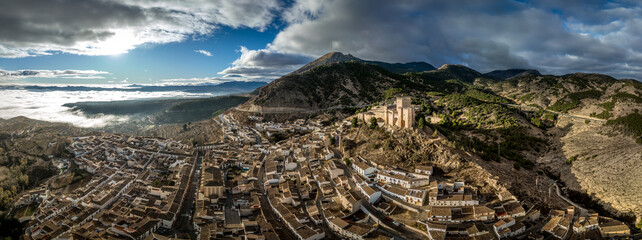 Wall Mural - Aerial view of  Velez Blanco castle on a hilltop and town with one or two floor houses whitewashed walls and tiled roofs with dramatic cloudy sky in Andalusia Spain