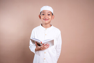 Wall Mural - Young Asian Muslim boy wear skullcap holding holy book of Quran 