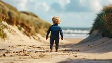 Rear View Of A Little Boy In Wetsuit Walking Along The Beach
