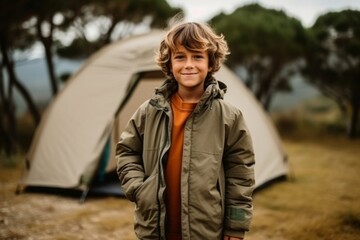 Wall Mural - Portrait of a cute boy standing in front of a tent in the countryside