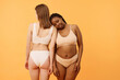 © AnnaStills - Conceptual studio shot of two young ethnically diverse women wearing minimalistic lingerie posing for camera, warm apricot background