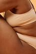 © AnnaStills - Vertical side view crop shot of unrecognizable young Black woman with curvy body wearing minimalistic underwear sitting in studio