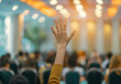 © ChanelBot/Peopleimages - AI - Raised hand, people and audience asking or voting at business meeting, conference or trading seminar. Hall, closeup and back view for convention, workshop gathering, or ask a question in workplace