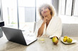 Work From Home. Woman Enjoys a Quiet Moment in a Bathrobe, With a Laptop and a Fresh Apple in Hand. The setting Suggests a Balance of Relaxation, Health.