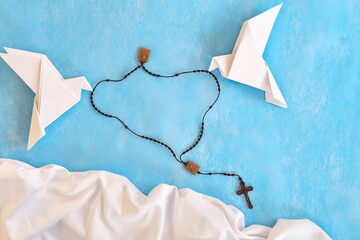 Wall Mural - White dove origami carrying rosary or scapular in sky blue background.