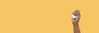 © TropicalNinjaStudio - Black male hand holding wireless headphones isolated on yellow banner.
