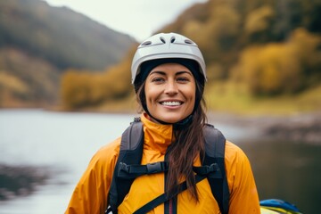 Poster - Happy young woman with backpack and helmet standing on the bank of a mountain river.