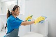 A woman in yellow rubber gloves meticulously wipes the restroom toilet seat with a cloth emphasizing importance of cleanliness and hygiene. Maid dedication is evident. Housekeeper healthcare concept