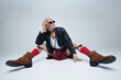 © Lustre Art Group  - Young man with sunglasses dressed traditional Scottish attire and modern leather jacket posing sitting against grey studio background. Concept of fashion fusion, art photography, self-expression. Ad