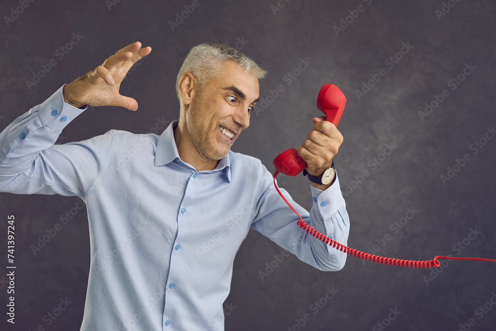 Angry furious Caucasian man on black studio background talk on corded ...