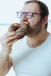 © dturphoto - Man with excess weight eat chocolate donut, unhealthy snack for lunch. Sugar addiction and problems with overweight