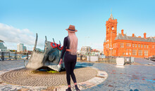 A Beautiful Blonde Woman With A Stylish Hat Wearing Black Tight Trousers Walking On The Street  - Merchant Seafarers’ War Memorial - Cardiff, Wales