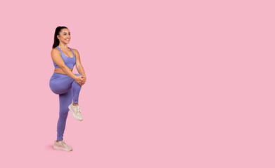 Wall Mural - Smiling young woman performing leg stretch on pink background