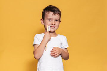 Wall Mural - A smiling boy with healthy teeth holds a plus tooth and a toothbrush on a isolated background. Oral hygiene. Pediatric dentistry. Prevention of caries.